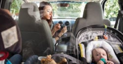 A woman smoking in her car with a baby in the backseat causing secondhand smoke