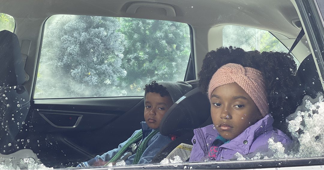 Two young children in back seat of car looking out the window.